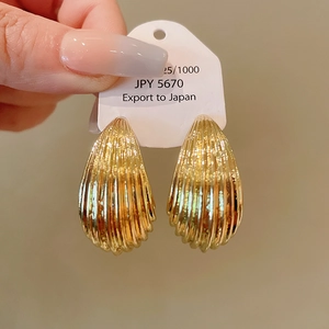 Macro shot of gold shell earrings with vertical textures and polished metallic finish