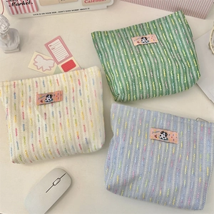 Three knit cosmetic bags in cream, green, and blue with vertical colorful stripes