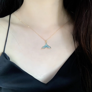 Goldene Halskette mit blauem Walflossen-Anhänger an einem Model vor schwarzer Kleidung