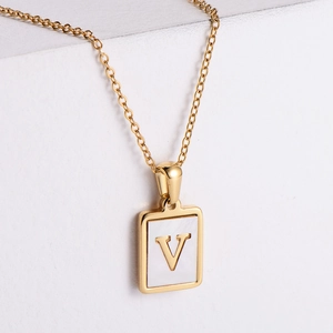 Macro view of 18k gold plated square pendant with white shell inlay and letter V initial