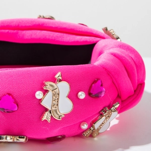 Détail du serre-tête noué rose fuchsia avec strass en cœur et boucle flèche LOVE dorée