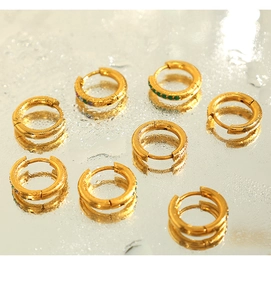Macro detail of gold hoop earrings with green zircon stones on reflective water surface
