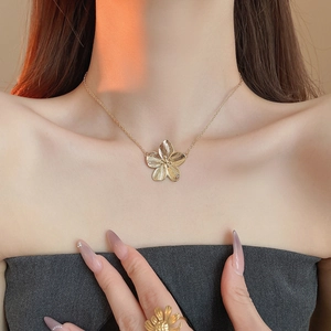 Macro detail of golden brushed flower necklace and matching daisy ring on a model