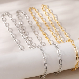 Close-up of gold and silver paperclip chains hanging on a white cylinder with soft shadows