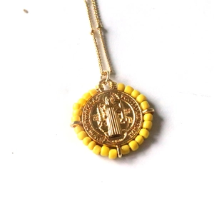 Macro shot of Saint Benedict gold pendant with yellow beads and detailed engraving