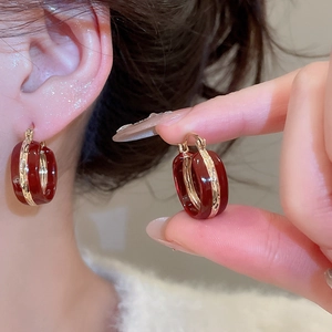 Close-up of burgundy enamel C-shape hoop earrings with textured gold metallic inlay detail