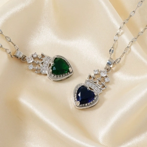 Detailed shot of heart-shaped crown pendants in emerald and sapphire colors on silk