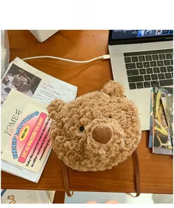 Detailed view of a cute brown plush bear-shaped crossbody bag on a cozy office desk
