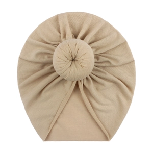 Detail of beige soft cotton baby donut hat with decorative top knot bun texture