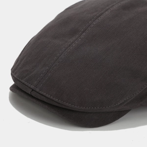 Detail shot of the charcoal grey newsboy cap showing fine stitching and twill fabric texture