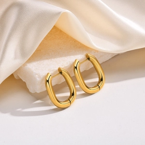 Close-up of polished gold U-shape hoop earrings placed on elegant white textured stone