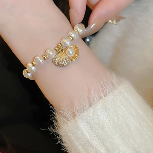 Macro detail of a pearl bracelet featuring a gold shell charm set with sparkling zircons
