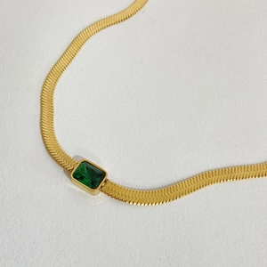 Close-up of a gold snake chain necklace featuring a radiant green rectangular gemstone