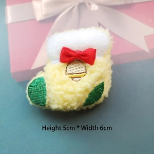 Close-up of a plush yellow Christmas stocking brooch with red bow and white pom-poms