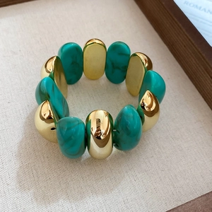 Detail of acrylic tortoiseshell and gold oval bead bracelet on a beige linen tray