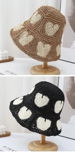 Detail of hand-crocheted raffia straw hats with white heart patterns in brown and black