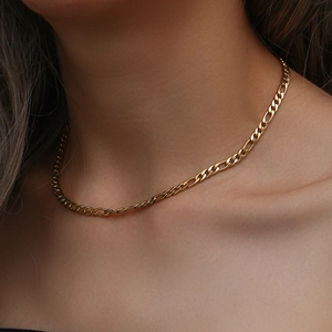 Primo piano di una collana a catena Figaro dorata indossata da una modella con finitura lucida