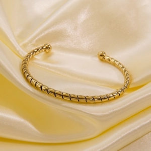 Detailed view of gold twisted cuff bangle with ball ends on elegant yellow satin silk