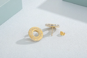 Detailed shot of gold stud earrings featuring a crystal circle and MOM engraved disk