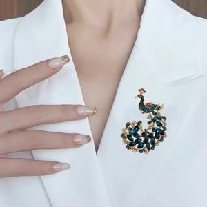 Elegant peacock brooch with colorful crystals on a white blazer, gold base animal pin