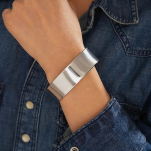 Close-up of wide polished silver metal open cuff bracelet on a denim jacket sleeve