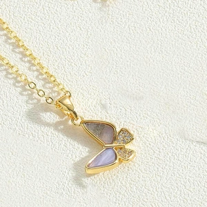 Macro shot of gold butterfly pendant with purple and grey wings and zircon inlay