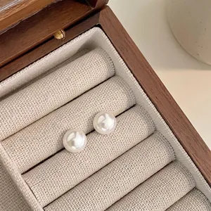 Close-up of elegant white pearl earrings on a textured linen display in a wooden box