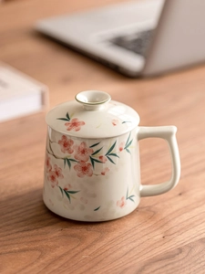 Close-up of ceramic tea mug with hand-painted peach blossoms and bamboo on wooden desk