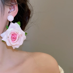 Close-up of oversized pink fabric rose earrings with green leaves worn by a model
