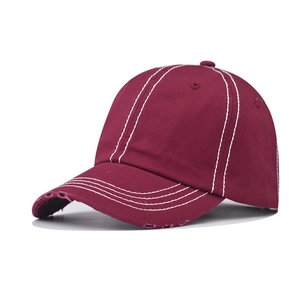 Detail of burgundy washed cotton baseball cap with white contrast stitching and distressed brim