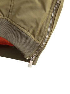 Detail of army green bomber jacket with metal zipper, orange lining and ribbed hem