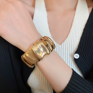 Gros plan d'un large bracelet manchette doré avec une texture métallique ondulée polie
