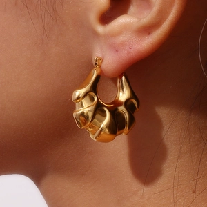Close-up of golden textured hollow earring worn by a model showing luxury metallic finish