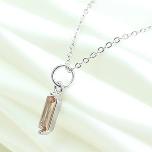 Close-up of champagne rectangle gemstone pendant with silver chain on fabric background