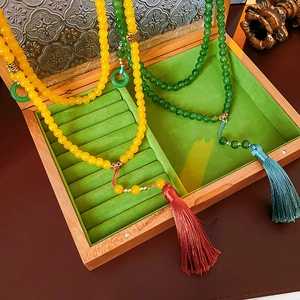 Détail de colliers à pompons perlés vert et jaune dans une boîte à bijoux en velours