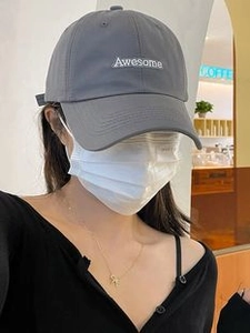 Detail view of a gray baseball cap with Awesome embroidery on a model in a cafe setting