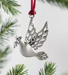 Macro detail of silver tin dove metal ornament with red ribbon on green pine branch