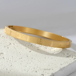 Detail of gold titanium steel bangle with grid texture and religious medal engravings