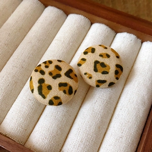 Macro shot of circular leopard print earrings with a soft fabric texture in a beige tray