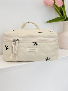 Quilted off-white cosmetic bag with black bow embroidery and top handle for travel