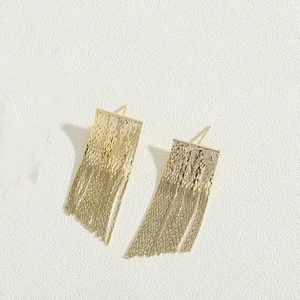 Detailed macro view of gold tassel earrings with intricate textured diamond-patterned metal