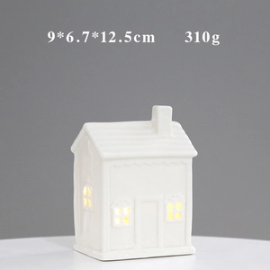 Detail view of a white ceramic house ornament with warm LED light and hollow design