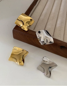 Detail of gold and silver irregular twisted wave stud earrings with metallic mirror finish