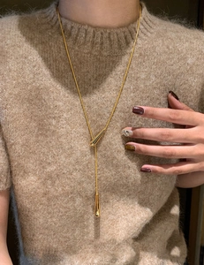 Detailed view of golden teardrop pendant on snake chain worn over a brown knit sweater