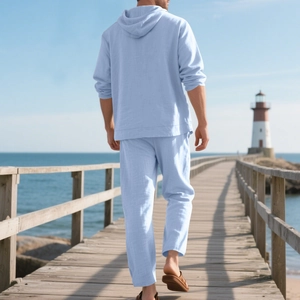 Rear view of a man in light blue linen hooded shirt and pants set on a scenic beach pier