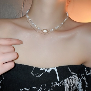 Detail of a gold double-layer necklace featuring white pearls and a crystal pendant