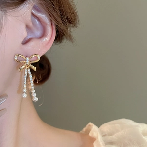 Detail of elegant gold-plated bow earrings with dangling pearls and zircon accents