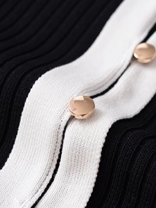 Detail of ribbed knit texture and polished gold metal button on a black and white cardigan