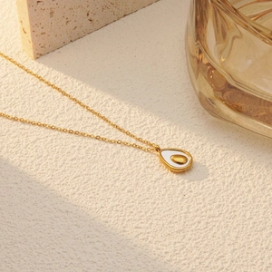 Detail shot of a golden avocado pendant necklace with white enamel inlay on stone