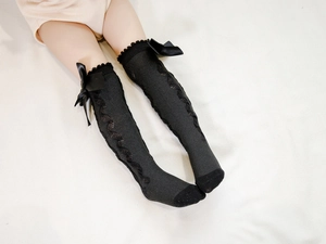 Detail of knee-high baby socks with double bows and cable knit patterns in black